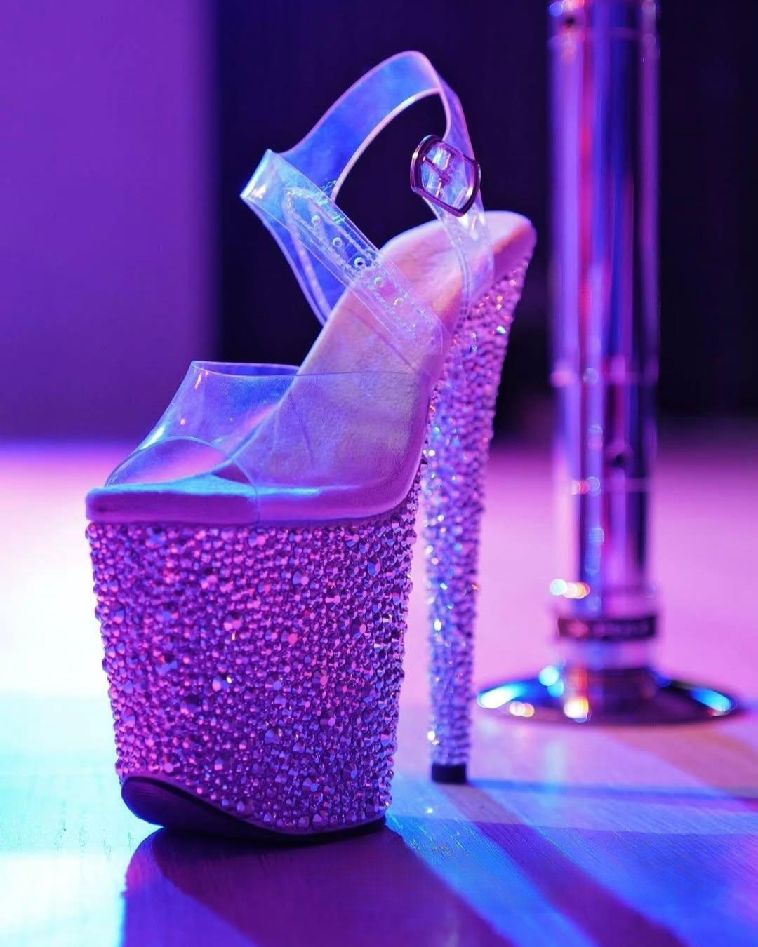 High-heeled shoe with crystal embellishments on a reflective surface with purple lighting